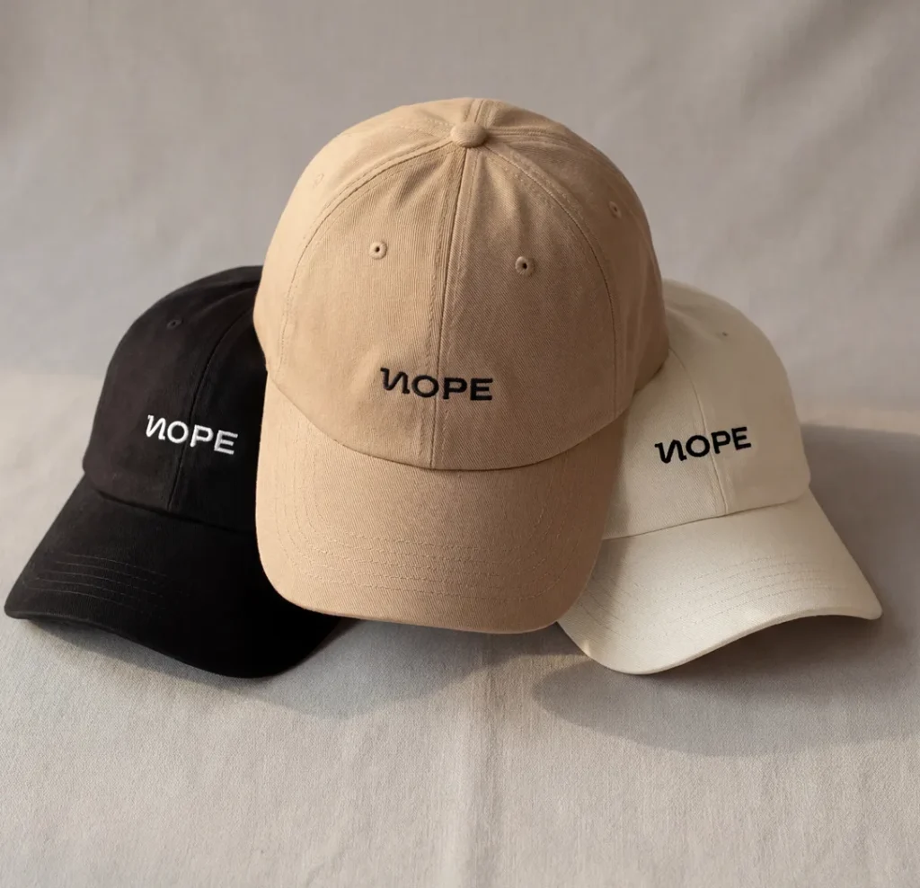 Gorras de merchandising de NOPE con el logotipo bordado, en negro, camel y crudo
